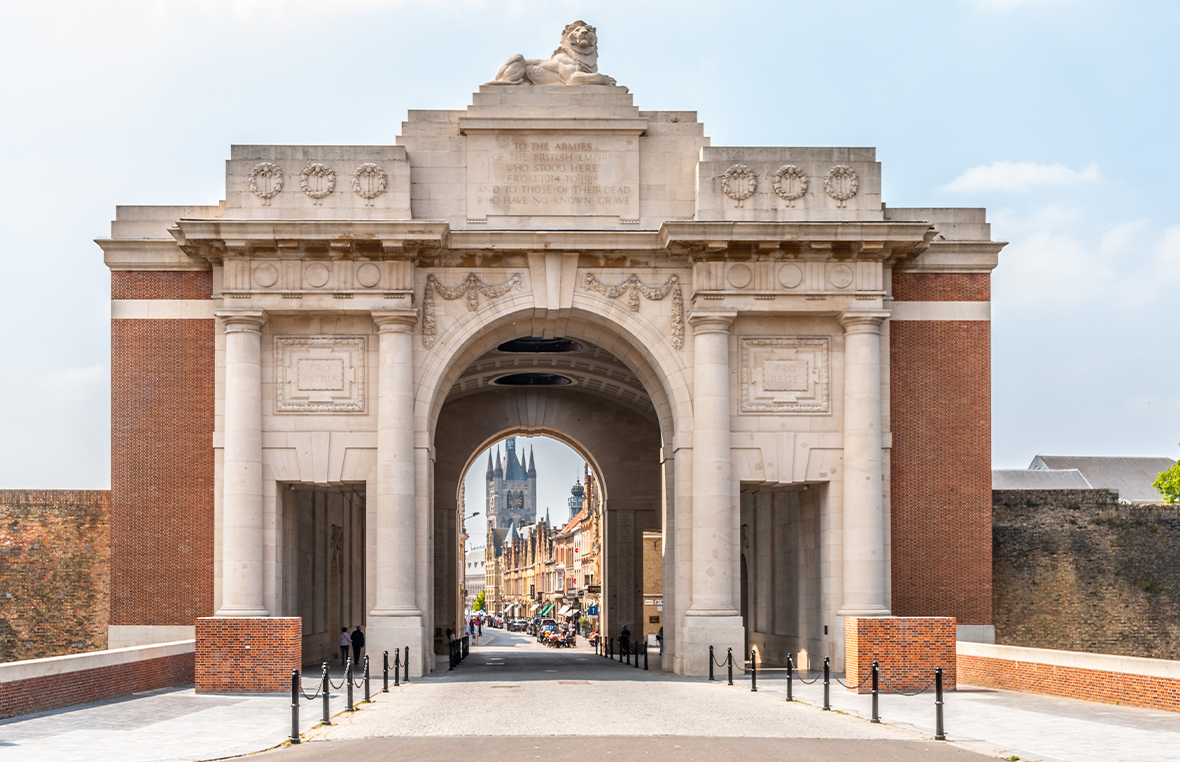 Large white stone archway with a view of a pretty city beyond it standing as part of a large brick wall